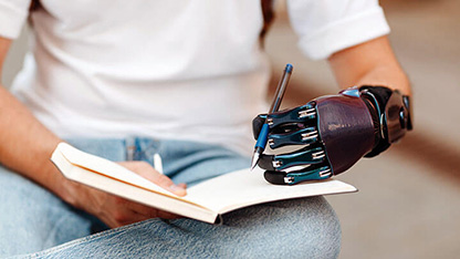 Una persona escribiendo en un cuaderno con una mano protésica sujetando el bolígrafo.