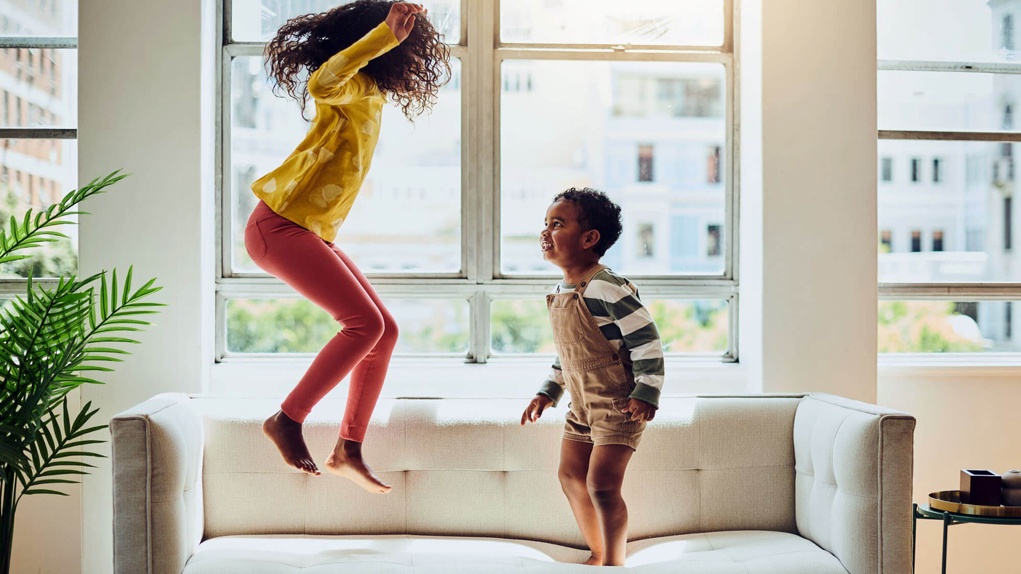 Happy siblings are jumping on the sofa in their living room with copy space